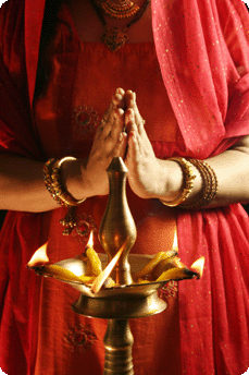 Indian woman holding her hands together in prayer infront of burning candles